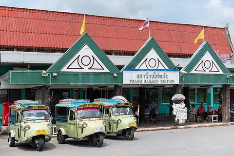Three pale green three-wheeled taxis parked in front of a station building with green gables and a red roof. Opens a larger view