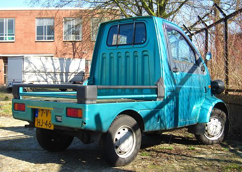 Rear of a turquoise tiny pickup with a ribbed cab back, grab rails and a yellow Dutch plate on gravel. Opens a larger view