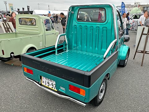 Rear of a turquoise tiny pickup with a black bed rail and Japanese plate, a pale green one behind. Opens a larger view