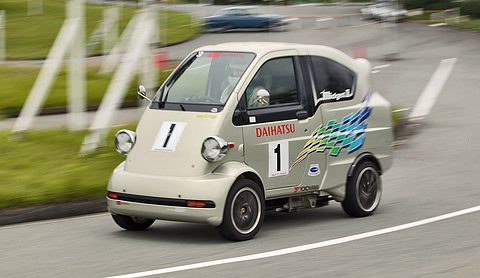 Silver tiny van with DAIHATSU lettering and race number 1 cornering on a track, the background blurred by panning. Opens a larger view