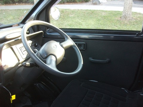 Grey two-spoke steering wheel and plain dashboard in front of a single black seat, seen through the door.