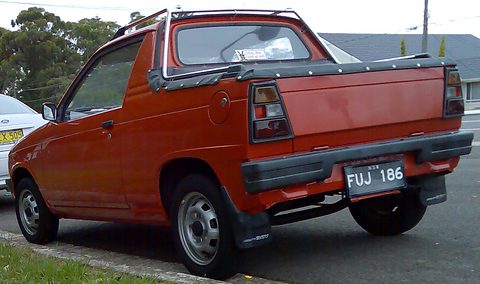 Rear quarter of a red small coupé-utility with a roll bar over its bed, a black bumper and an Australian plate, at a kerb. Opens a larger view
