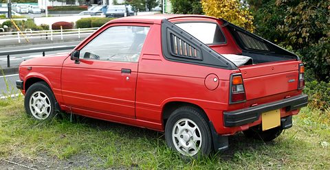 Rear quarter of a red small coupé-utility with a short bed, a black bed cover and a roll bar, on grass by a road. Opens a larger view