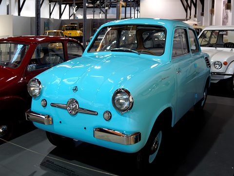 Bright blue small saloon with chrome bumpers on a dark plinth between a red and a white car. Opens a larger view