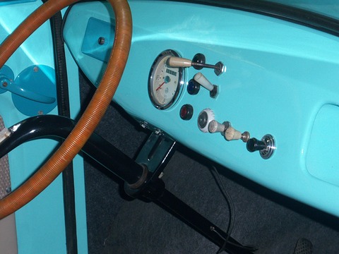Turquoise painted dashboard with one round speedometer, toggle switches and a brown steering wheel rim. Opens a larger view