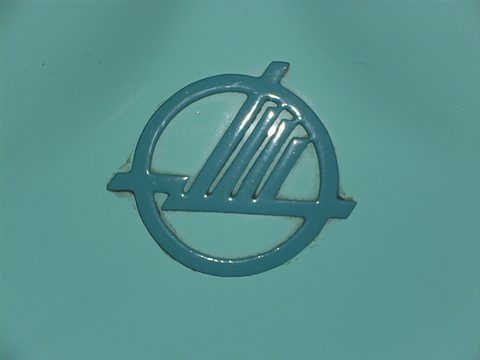 Raised circular emblem with stylised wings, painted in the same turquoise as the body. Opens a larger view