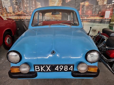 Blue small car head-on with plate BKX 4984, a city-night mural behind. Opens a larger view