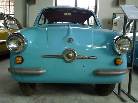 Sky-blue small car facing the camera: round headlamps, chrome nose bar and amber indicators. Opens a larger view