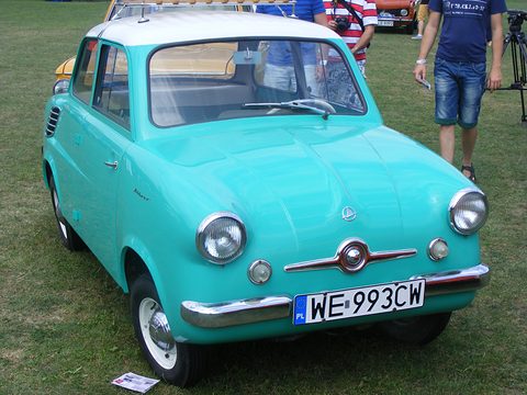Turquoise small car with a white roof and Polish plate WE 993CW on grass, visitors behind. Opens a larger view