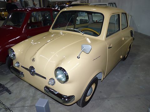 Cream small saloon with a chrome mirror on its wing, on a concrete floor beside a red car. Opens a larger view