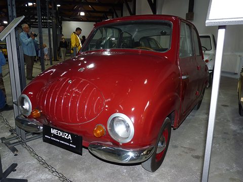 Dark red small four-door saloon with an oval dummy grille, a MEDUZA plate and a chain barrier.