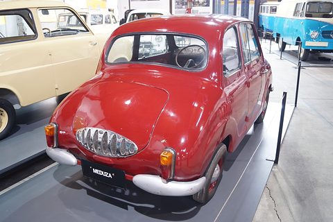 Red small saloon from behind with a chrome oval grille on the tail and a MEDUZA plate. Opens a larger view