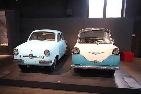 A pale blue saloon and a front-door two-tone microcar side by side on a dark plinth.