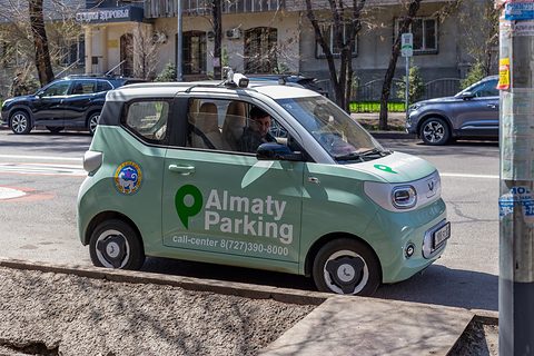 Pale green boxy city car with Almaty Parking lettering and a roof light, parked at a street corner. Opens a larger view
