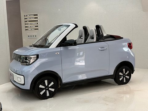 Pale blue open two-seater with white roll hoops and black wheels on a white showroom floor. Opens a larger view