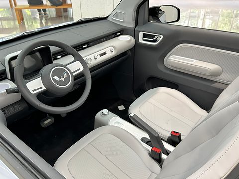 Two pale grey seats, a two-spoke steering wheel and a grey dashboard seen from above an open car. Opens a larger view