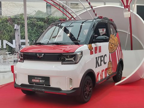 White and red boxy city car with KFC lettering and a fried-chicken graphic on a red carpet under a white arch. Opens a larger view