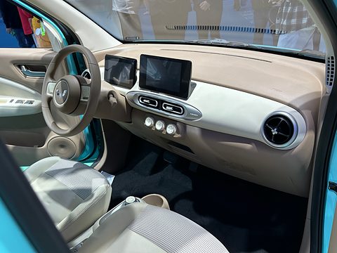 Beige and white dashboard with two separate screens, a round vent and a two-spoke steering wheel. Opens a larger view