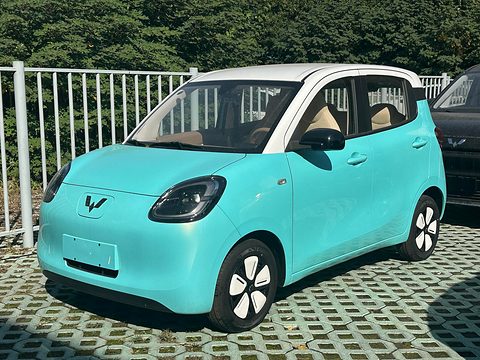 Turquoise rounded small hatchback with round headlamps and a white roof, parked on grass pavers by a white fence. Opens a larger view