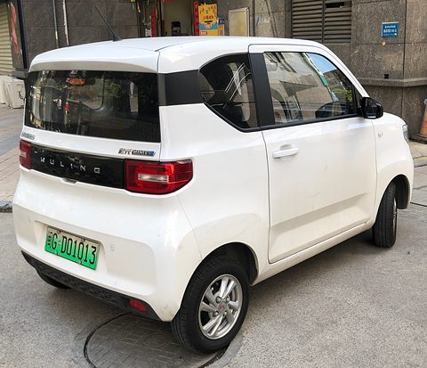 Rear of a white boxy city car with a black tailgate band and Wuling lettering, a green plate, parked by a building. Opens a larger view