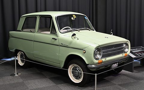 Pale green small saloon with whitewalls on a dark carpet in front of black drapes. Opens a larger view