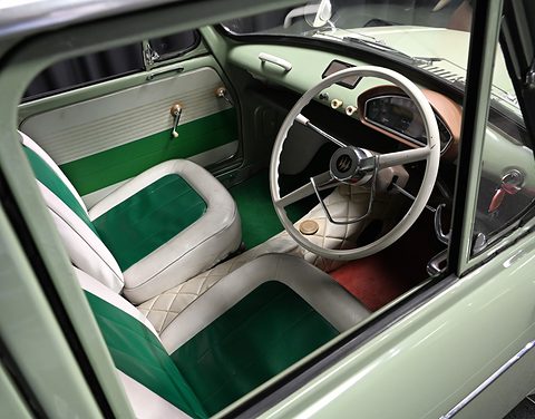 Through an open door: green and white seats, a thin white two-spoke wheel and a pale green dashboard. Opens a larger view