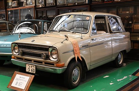 Cream small saloon with a cloth over its wing, on a green floor in front of wooden display cases. Opens a larger view