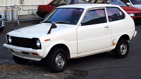 White small hatchback with black grille and square headlamps, parked by a gas-bottle store. Opens a larger view