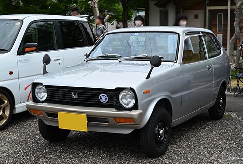 Silver small hatchback with a black grille on gravel, a white car beside it. Opens a larger view