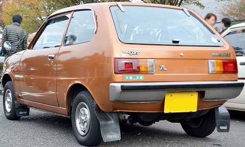 Rear three-quarter of a copper hatchback with mudflaps, people walking past behind. Opens a larger view