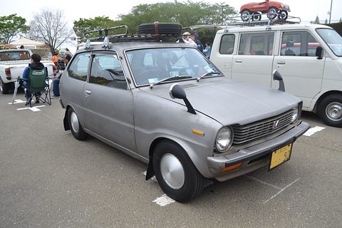Silver small hatchback with a black roof rack carrying a toy car, a white van behind. Opens a larger view