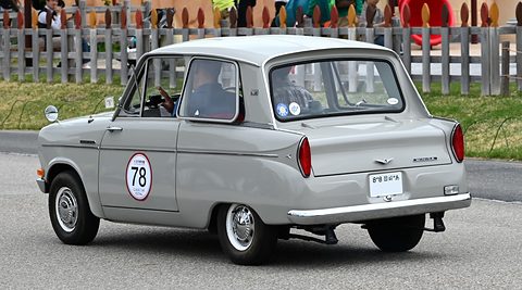 Rear three-quarter of a pale grey saloon with a number 78 roundel, a wooden fence behind. Opens a larger view