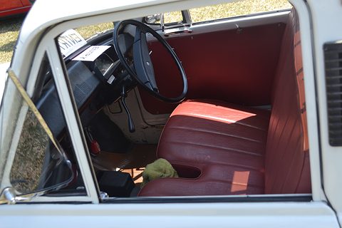 Through an open door: a red bench seat, a large black steering wheel and a white door frame. Opens a larger view