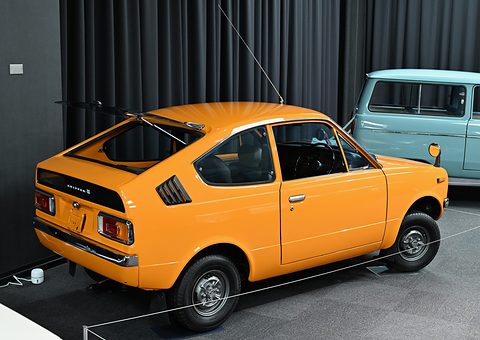 Rear three-quarter of an orange coupé with a cut-back rear window and side vents.