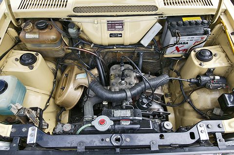 Cream-painted engine bay with a small engine, a battery and hoses. Opens a larger view