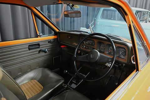 Through an open door: a three-spoke wheel, a brown fascia with round dials and black seats. Opens a larger view