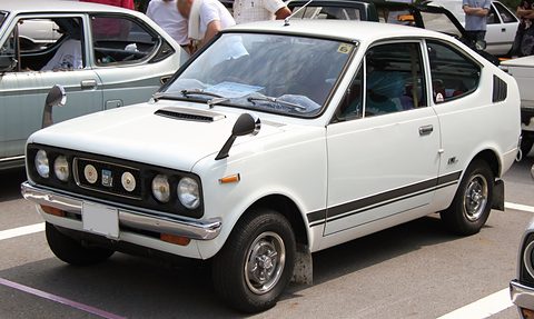 White small coupé with four headlamps, a bonnet scoop and a black side stripe. Opens a larger view