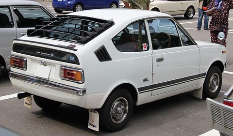Rear three-quarter of a white coupé with a louvred rear window and mudflaps. Opens a larger view