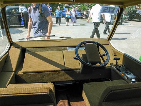 Brown cloth seats, a large steering wheel and a centre console under a wide windscreen. Opens a larger view