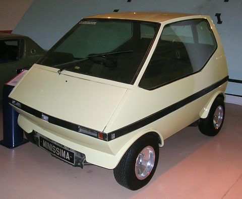 Cream boxy city car with a black waist stripe and a MINISSIMA plate on a museum floor. Opens a larger view