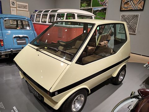 Cream boxy city car on a grey floor, a red-and-white van and a blue small car behind. Opens a larger view