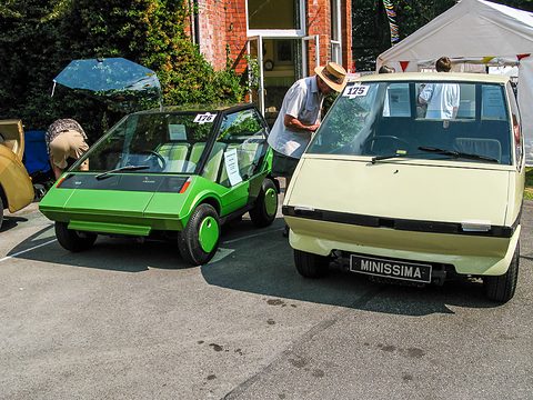 A green three-seat concept car beside the cream Minissima on a forecourt.