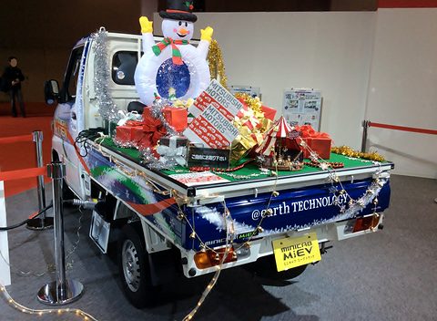 White kei pickup with its bed piled with gifts, tinsel and an inflatable snowman on a show stand. Opens a larger view