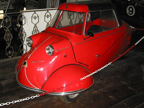 Red bubble car behind a chain barrier in front of a wrought-iron screen. Opens a larger view
