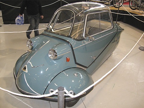 Blue-grey bubble car with clear canopy, roped off on a pale floor.