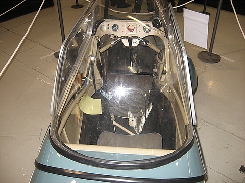 Looking down through the open canopy at a handlebar, instruments and two seats in line. Opens a larger view