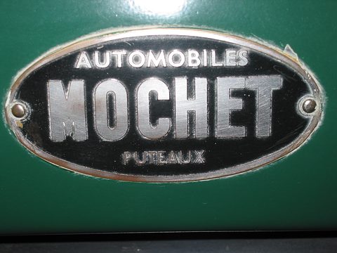 A black and chrome oval plate reading Automobiles Mochet Puteaux on green paint. Opens a larger view