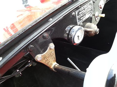 Close view of a black dash with an engraved maker’s plate, a small round dial and a gear lever. Opens a larger view