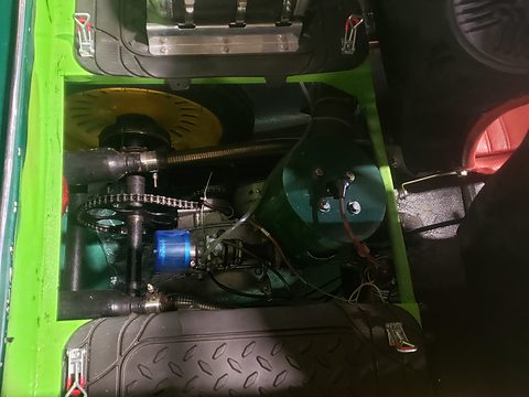 Dark engine bay between green panels showing a small engine, chain and sprocket. Opens a larger view