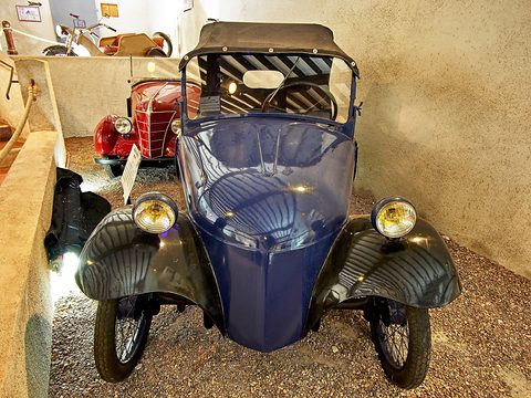 Front view of a small dark blue car with a pointed nose, black wings and two yellow lamps. Opens a larger view